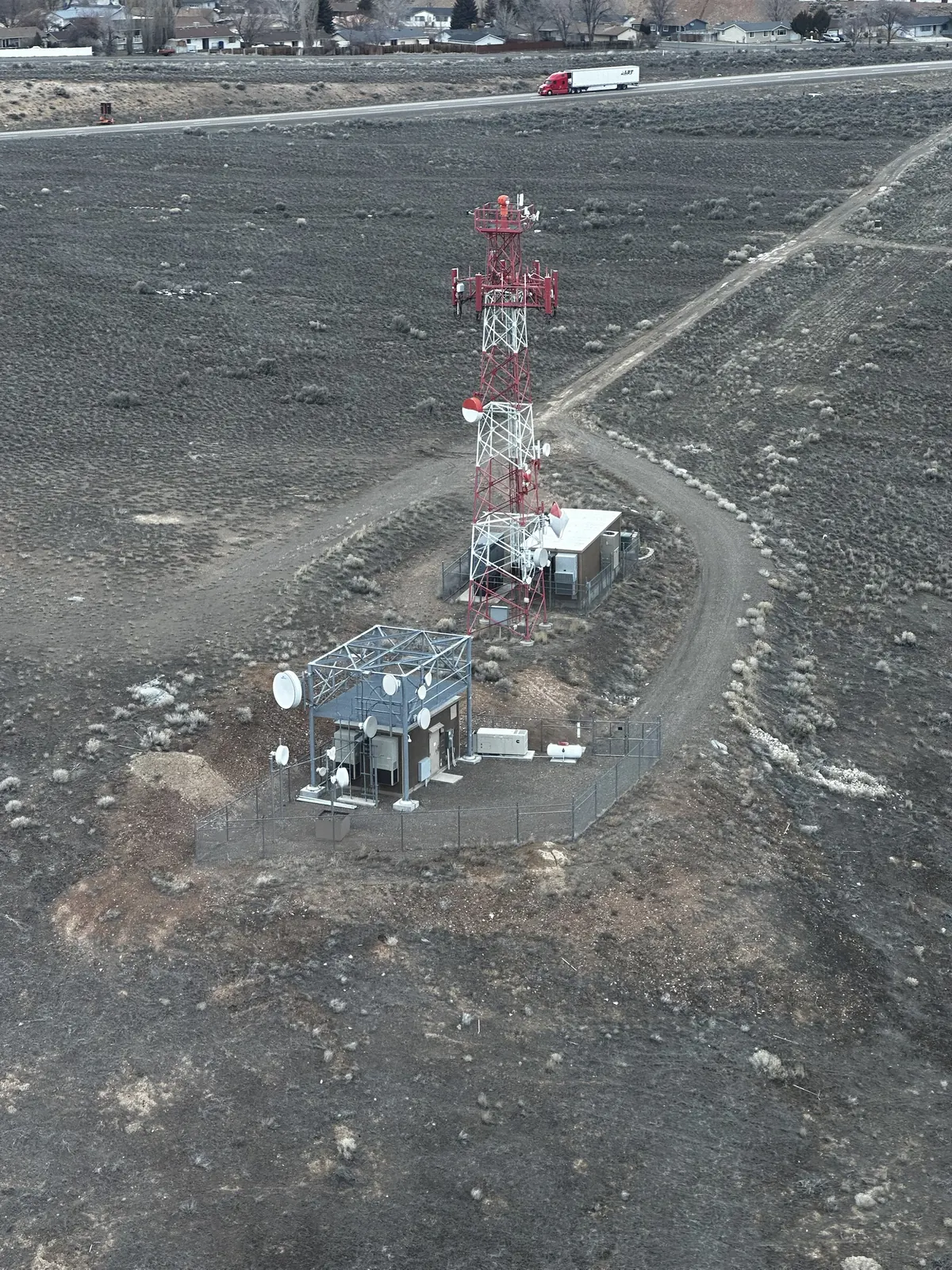 Aerial view of a red and white tower, shelters and fenced compound